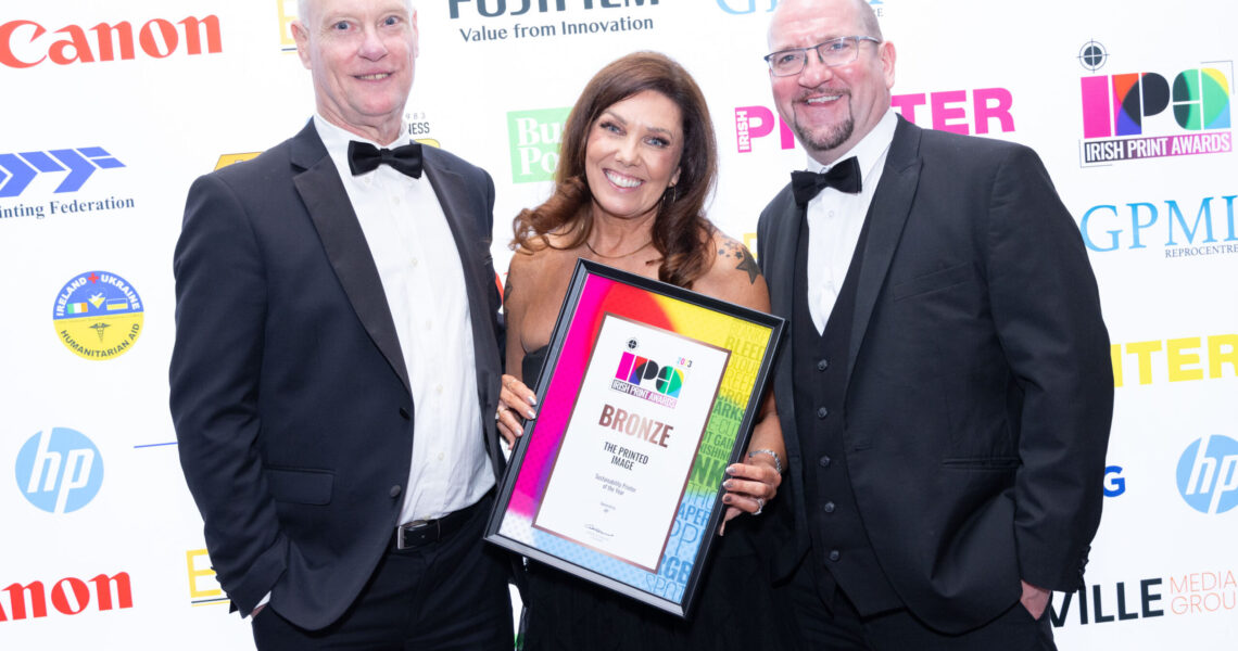 two men and 1 female smiling holding a print award