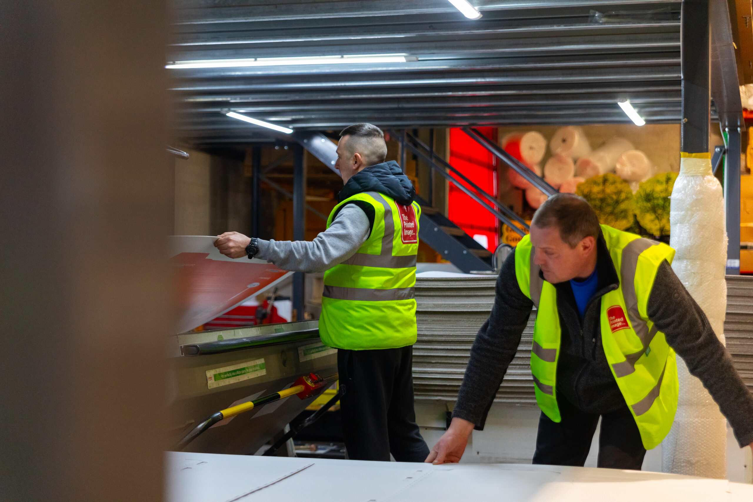 2 men in a high viz vest operating a printer